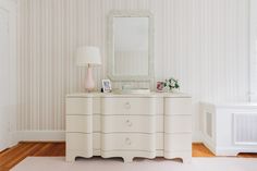 a white dresser sitting in the corner of a room next to a lamp and mirror