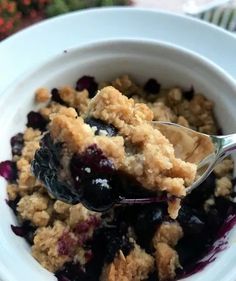 a spoonful of blueberry crumbler on top of a white bowl filled with oatmeal