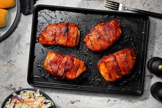 four pieces of bacon sitting on top of a black tray next to some oranges