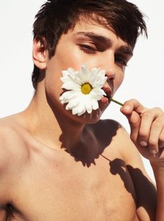 a shirtless man holding a flower in his mouth