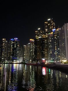 the city is lit up at night with lights reflecting in the water and skyscrapers