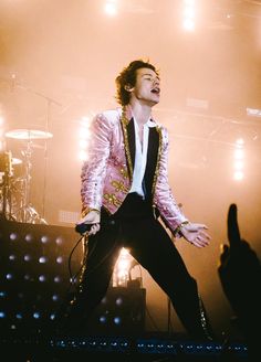 a male in a pink jacket and black pants on stage with his hands out to the side