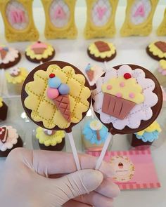 a person holding two lollipops in front of some cupcakes on sticks