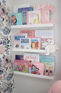 a white shelf filled with books next to a pink chair and wall mounted teddy bear