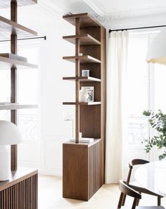 a room with a table, chair and bookcase in the corner next to a window