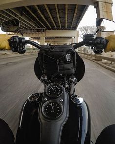 the handlebars and windshield of a motorcycle on a road under an overpass