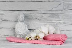 a buddha statue sitting next to a pink towel and white orchids in front of a brick wall