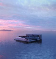 a couch sitting on top of a body of water under a pink and blue sky