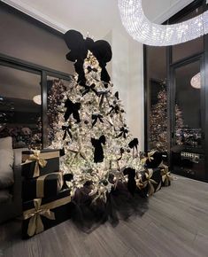 a decorated christmas tree with black and gold bows in a living room next to a large window