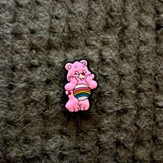 a pink teddy bear pin sitting on top of a gray carpeted floor next to a black wall