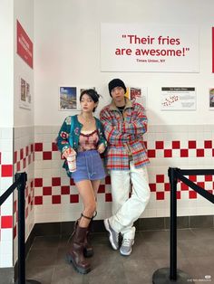 two people standing next to each other in front of a wall with red and white tiles