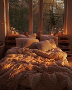 an unmade bed in front of a large window with candles on the windowsill