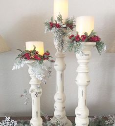 three white candles are decorated with holly and red berries