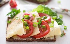 a sandwich with tomatoes, cheese and green onions on it sitting on a white surface