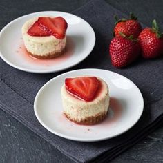 two white plates topped with mini cheesecakes and strawberries