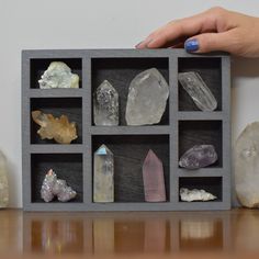 a person is holding a box with many rocks in it and there are other crystals on the table