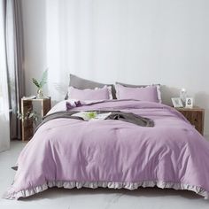 a bed with purple sheets and pillows in a white room