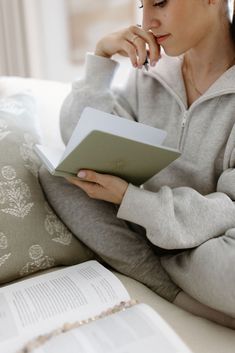 a woman sitting on a couch reading a book and looking at the page in her hand