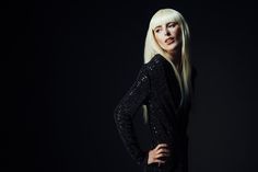 a woman with long blonde hair standing in front of a black background wearing a sequin dress