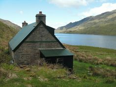 an old stone building sitting on top of a lush green hillside next to a lake