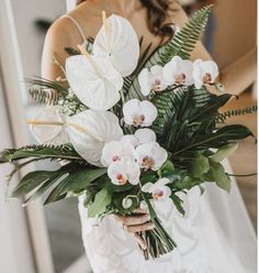 a bride holding a bouquet of white orchids and greenery for her wedding day