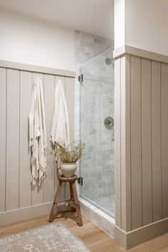 a bathroom with towels hanging on the wall next to a shower stall and wooden stool