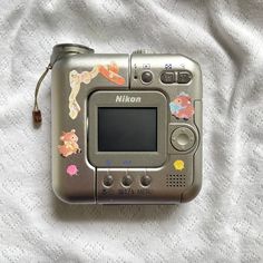 a digital camera sitting on top of a white bed sheet with stickers all over it