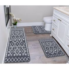 three bathroom rugs on the floor in front of a toilet