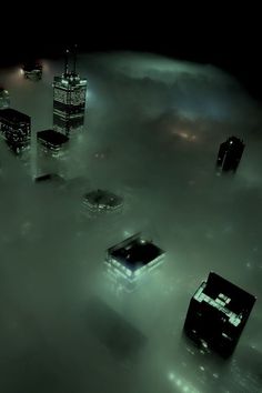 an aerial view of skyscrapers in the foggy sky at night with lights shining on them