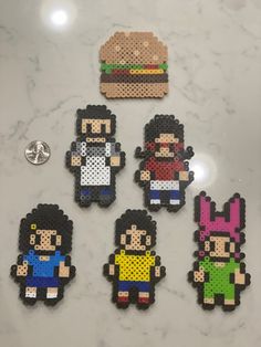 six pixelated characters are sitting on a counter top next to a button and pin