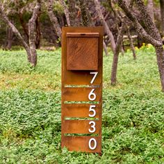 a sign that is in the grass near some trees and bushes with numbers on it