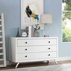 a white dresser sitting in a living room next to a lamp and painting on the wall