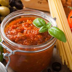 a glass jar filled with tomato sauce next to some pasta and other vegetables on a table