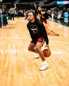 a man holding a basketball while standing on top of a hard wood floor in a gym