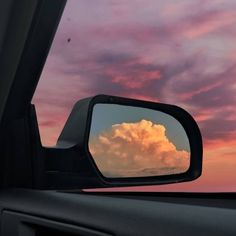 the clouds in the rear view mirror are pink and blue as the sun is setting