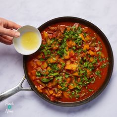 a pan filled with stew and vegetables being stirred by a person's hand holding a spoon