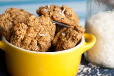 a yellow bowl filled with oatmeal cookies next to a jar of sugar