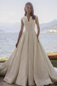 a woman in a wedding dress standing by the water with her hands on her hips