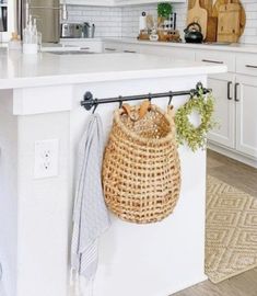 a kitchen with white cabinets and an island that has a basket hanging from it's side