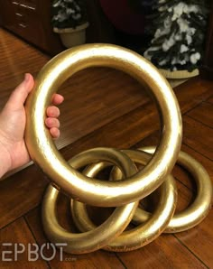 a hand is holding an object made out of metal rings on the floor in front of a christmas tree