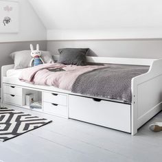 a white bed with drawers underneath it and a rug on the floor next to it