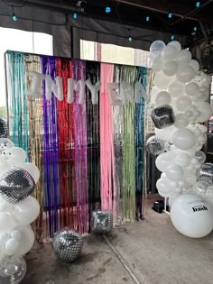 balloons and streamers are hanging from the ceiling in front of a wall with disco balls