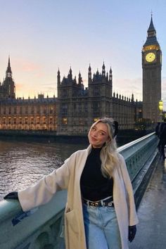 a woman standing on a bridge in front of the big ben clock tower at dusk