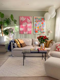 a living room filled with white furniture and paintings on the wall above it's windows