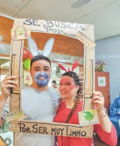 a man and woman pose for a photo in front of a wooden frame with bunny ears on it