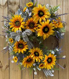 a wreath with sunflowers and other flowers on a wooden fence background, decorated with ribbon