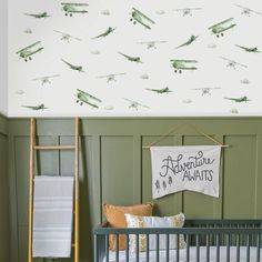 a baby's room with green and white wallpaper, an airplane themed rug, and a crib