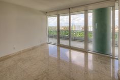 an empty living room with sliding glass doors leading to the balcony and cityscape in the background