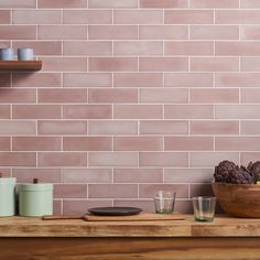 a wooden table topped with dishes and cups next to a brick wall covered in pink tiles