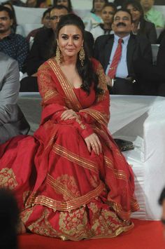 a woman in a red and gold dress sitting on a stage with other people behind her